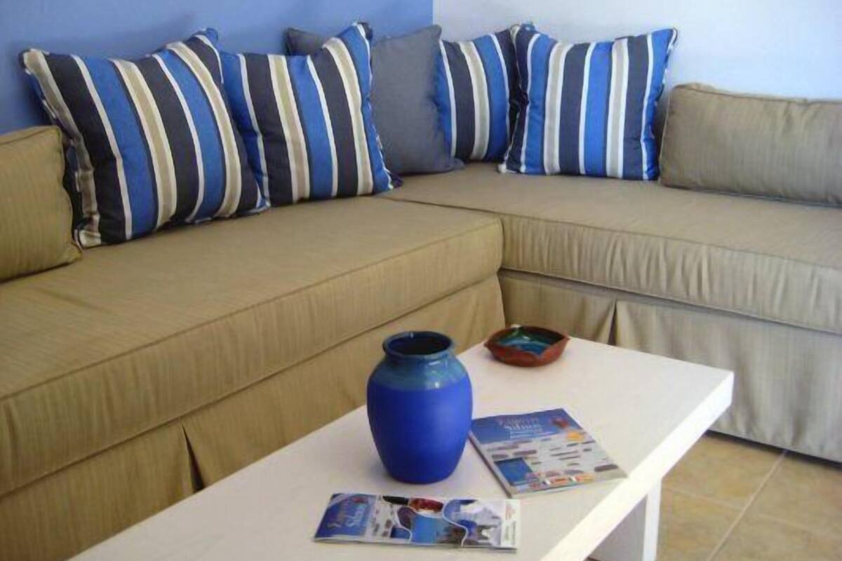 Un canapé beige agrémenté de coussins à rayures, une table blanche avec un vase bleu et des magazines, et un petit bol.