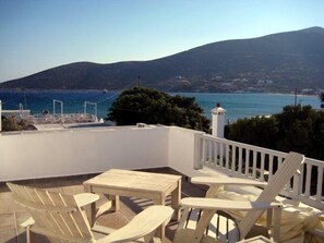 Una terraza con mobiliario blanco, vista al mar y una montaña al fondo.