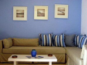 Ett rum med en beige soffa, ett vitt bord med en blå vas och tre inramade tavlor på väggen.