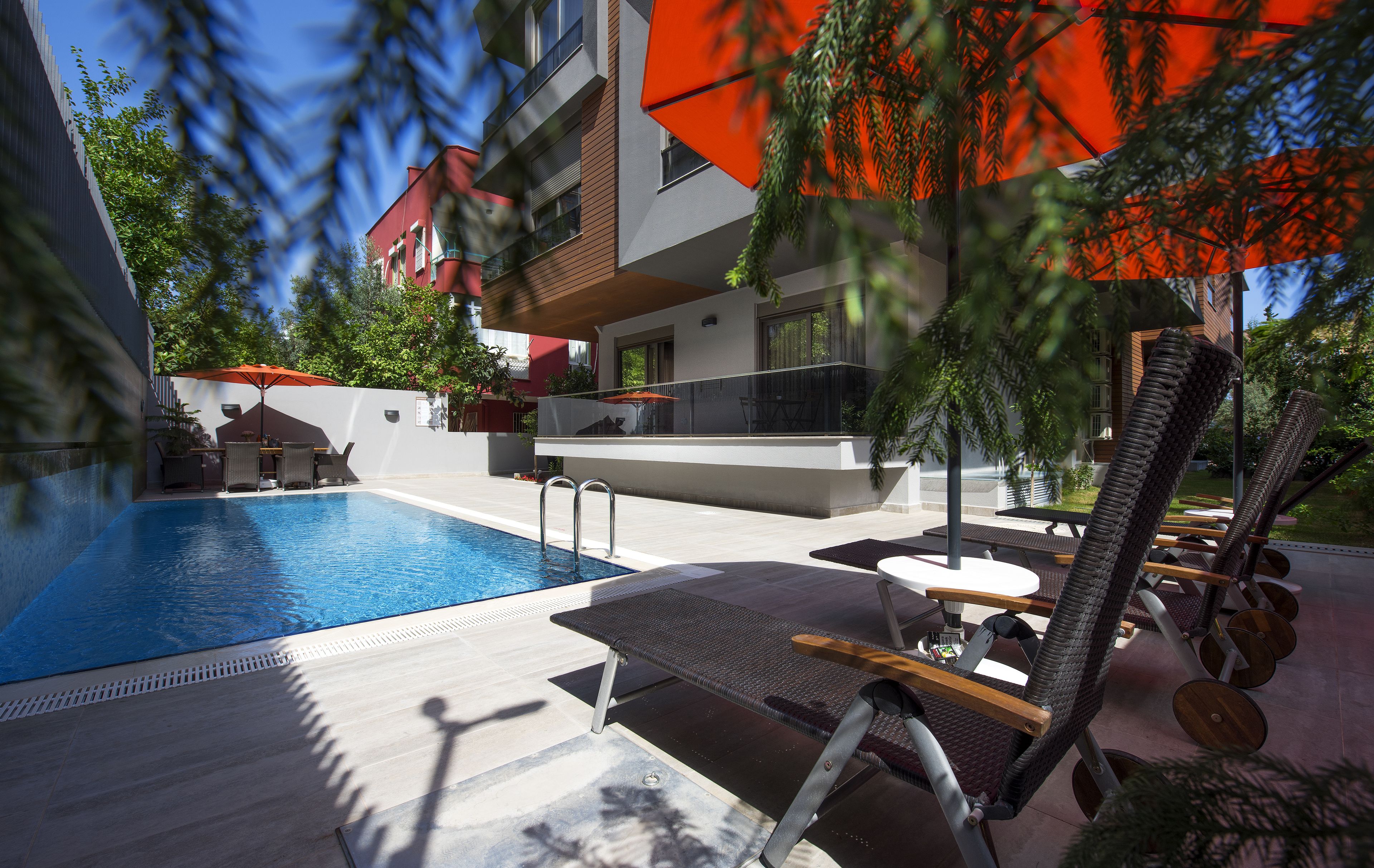 A swimming pool with lounge chairs and umbrellas, surrounded by a modern building with balconies.