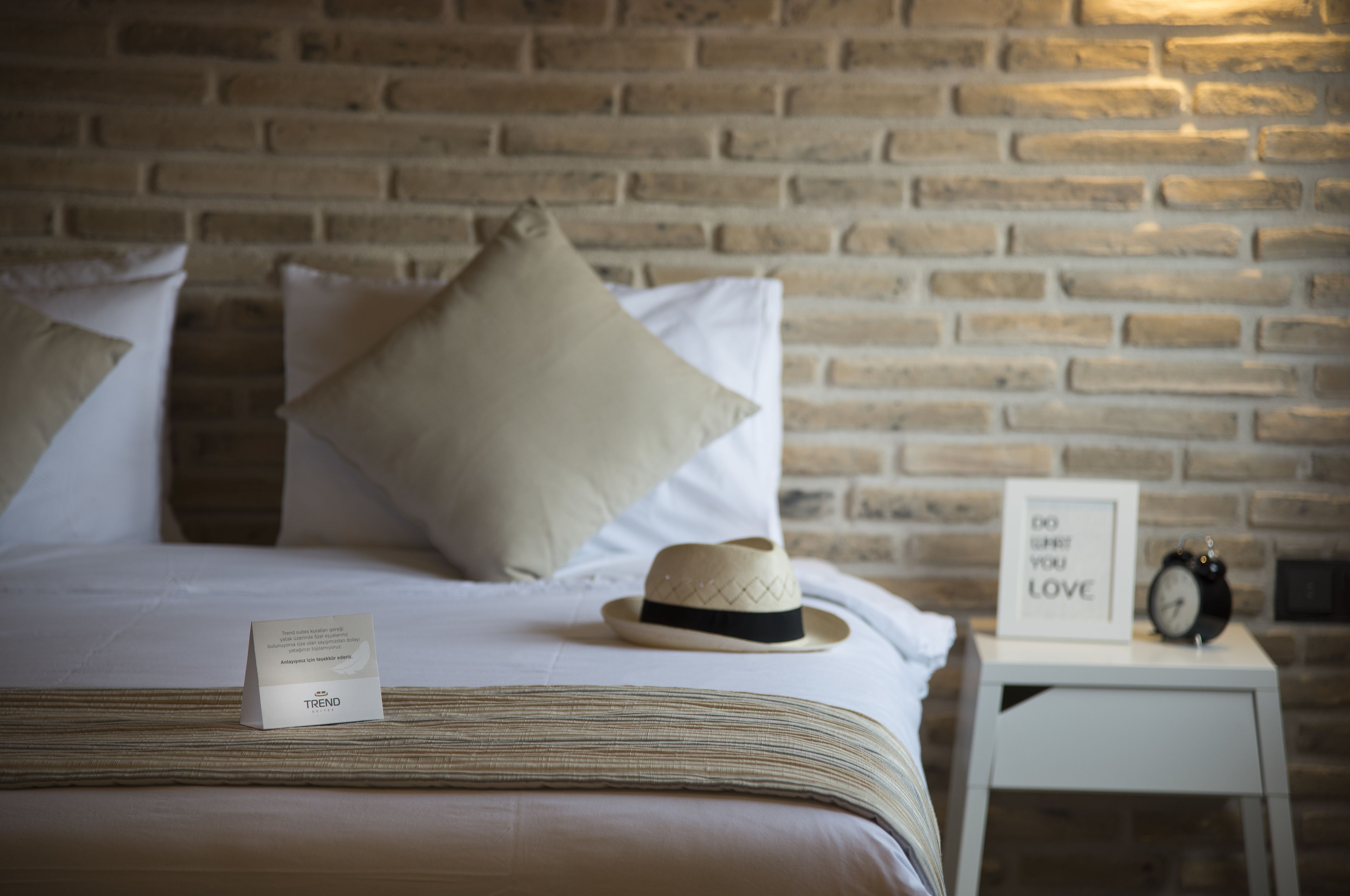 A neatly made bed with a striped bedspread, a beige hat, and a framed sign on a bedside table.