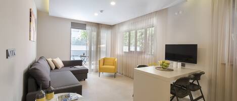 A modern living room with a sofa, a yellow armchair, a dining area with a TV, and a large window with curtains.