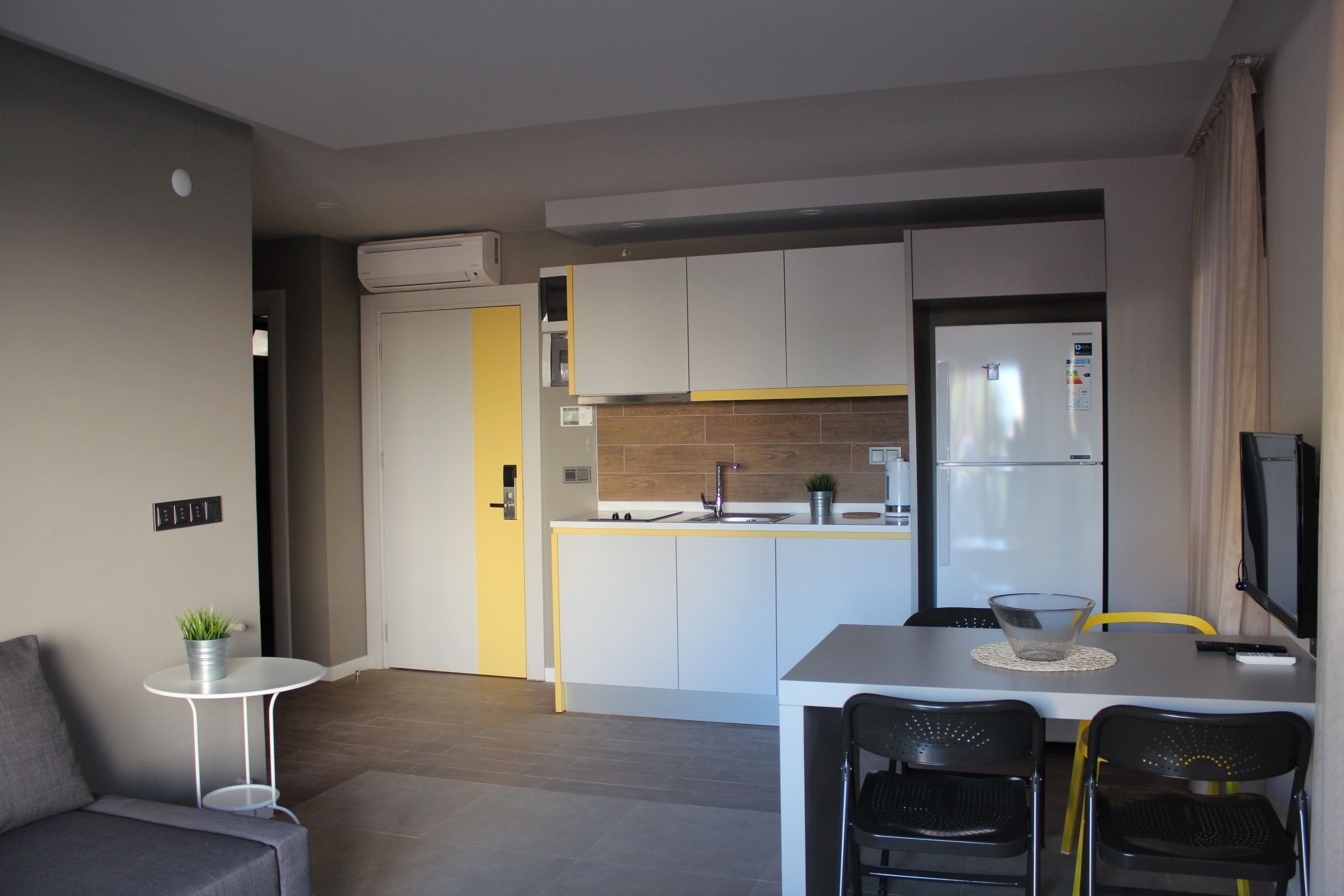 A modern kitchen with white cabinets, a stainless steel refrigerator, and a small dining area with a table and chairs.