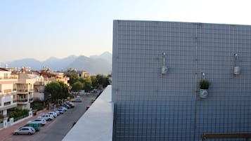 Un edificio moderno con fachada de diseño geométrico, una fila de coches aparcados y una vista despejada de montañas distantes.