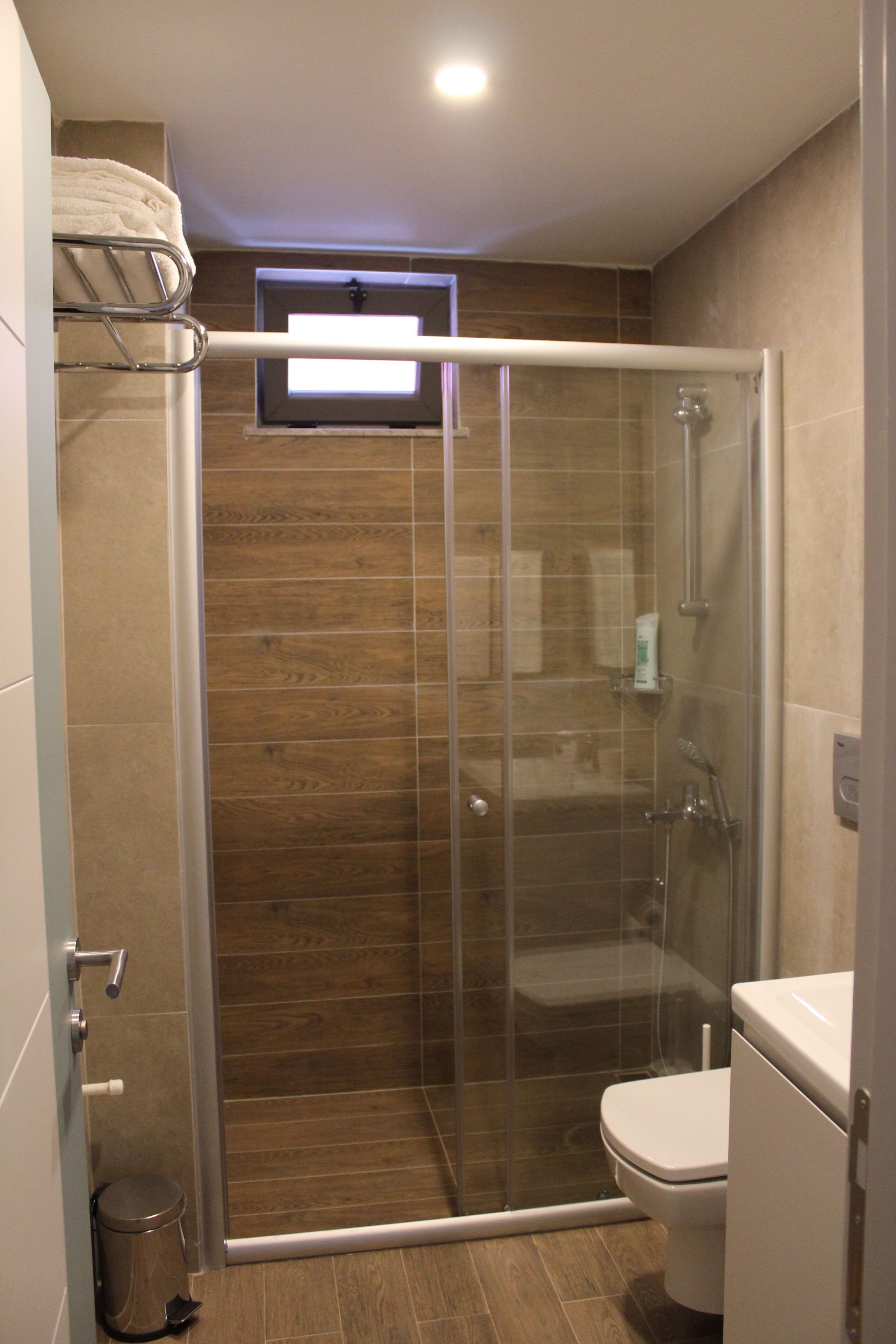 Een moderne badkamer met een glazen douchecabine, toilet en handdoekhouder.