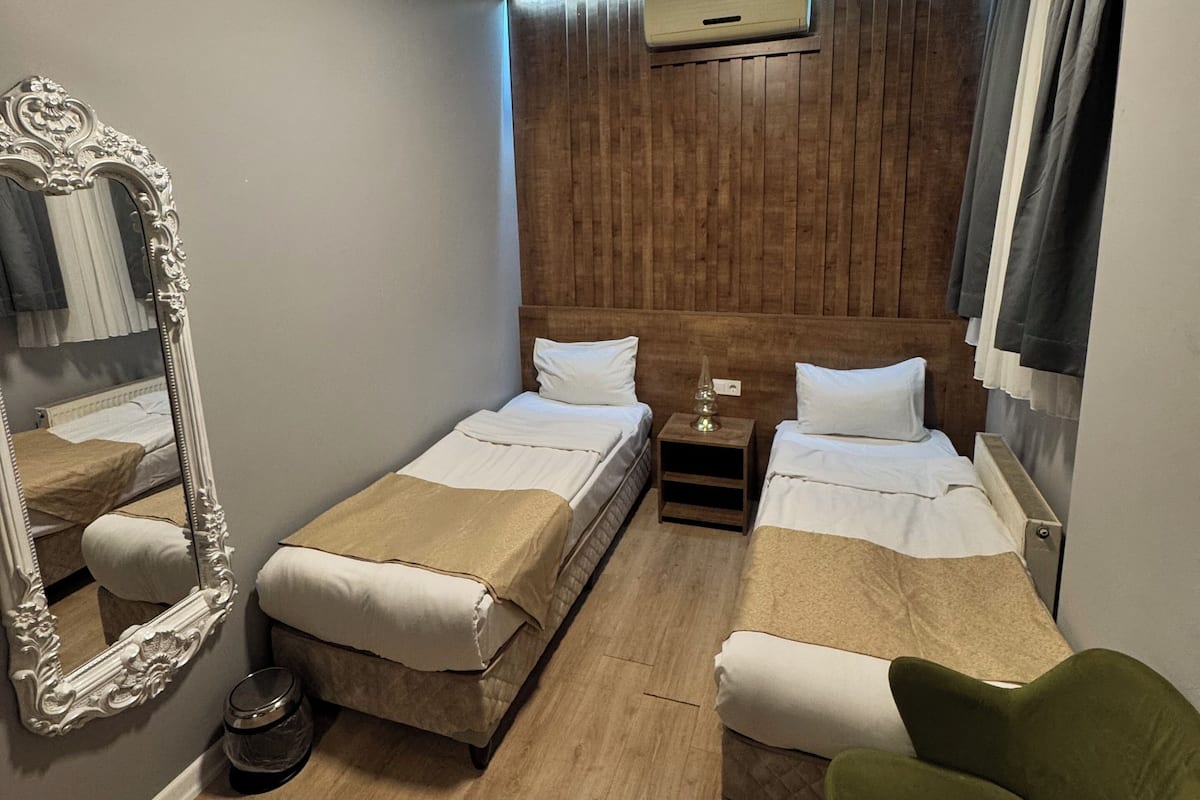 A hotel room with two single beds, a large mirror, a green chair, and a wooden headboard.
