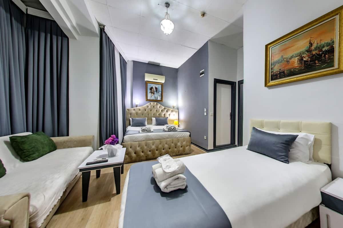 A hotel room with a bed, a sofa, a desk, and a painting on the wall.