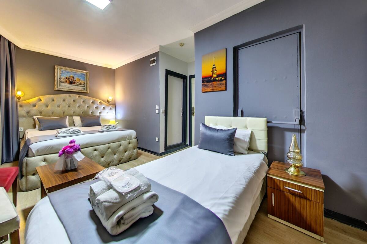 A hotel room with two beds, a wooden nightstand, a wall-mounted lamp, and a painting of a lighthouse.