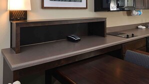 Ein Hotelzimmer mit Holzschreibtisch, Telefon, gerahmtem Bild an der Wand und einer Küchenzeile mit Mikrowelle und Spüle.