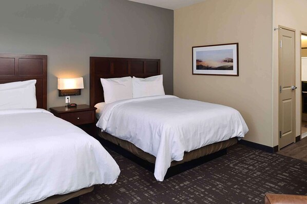 A hotel room with two beds, a nightstand with a lamp, a framed picture on the wall, and a door to a bathroom.
