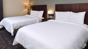 Ein Hotelzimmer mit zwei Einzelbetten, jeweils mit weißer Bettwäsche und einem hölzernen Kopfteil. Es gibt zwei Nachttische mit Lampen.