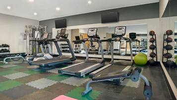 Un gimnasio con cintas de correr, máquinas de pesas y un espejo grande.