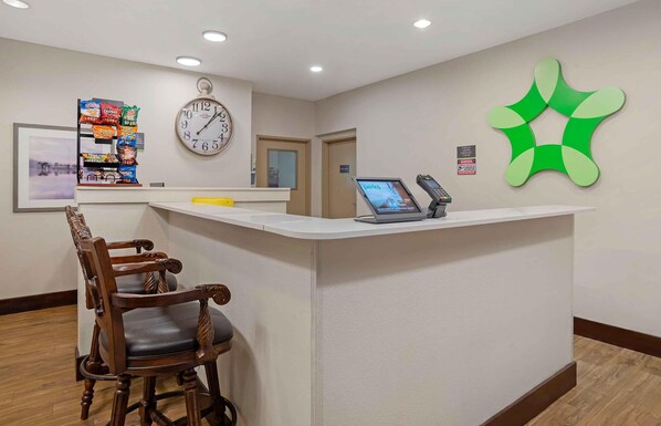 A reception desk with a clock, a computer, and a green wall decoration. - Extended Stay America Suites - Donaldsonville - Gonzales (St James)