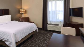 A hotel room with a bed, a desk, a chair, a television, and a window with curtains.