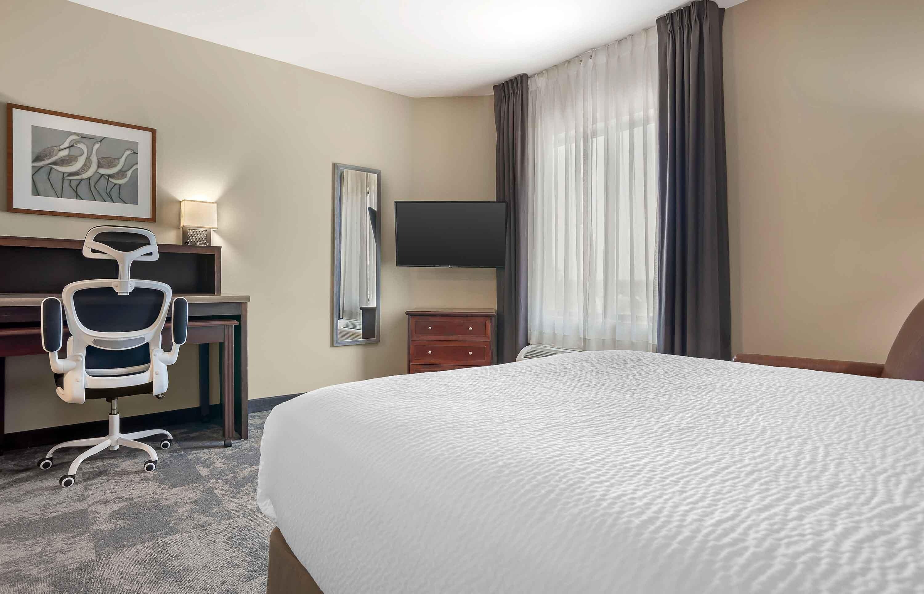 Habitación de hotel con cama, escritorio, silla, televisor y ventana con cortinas.