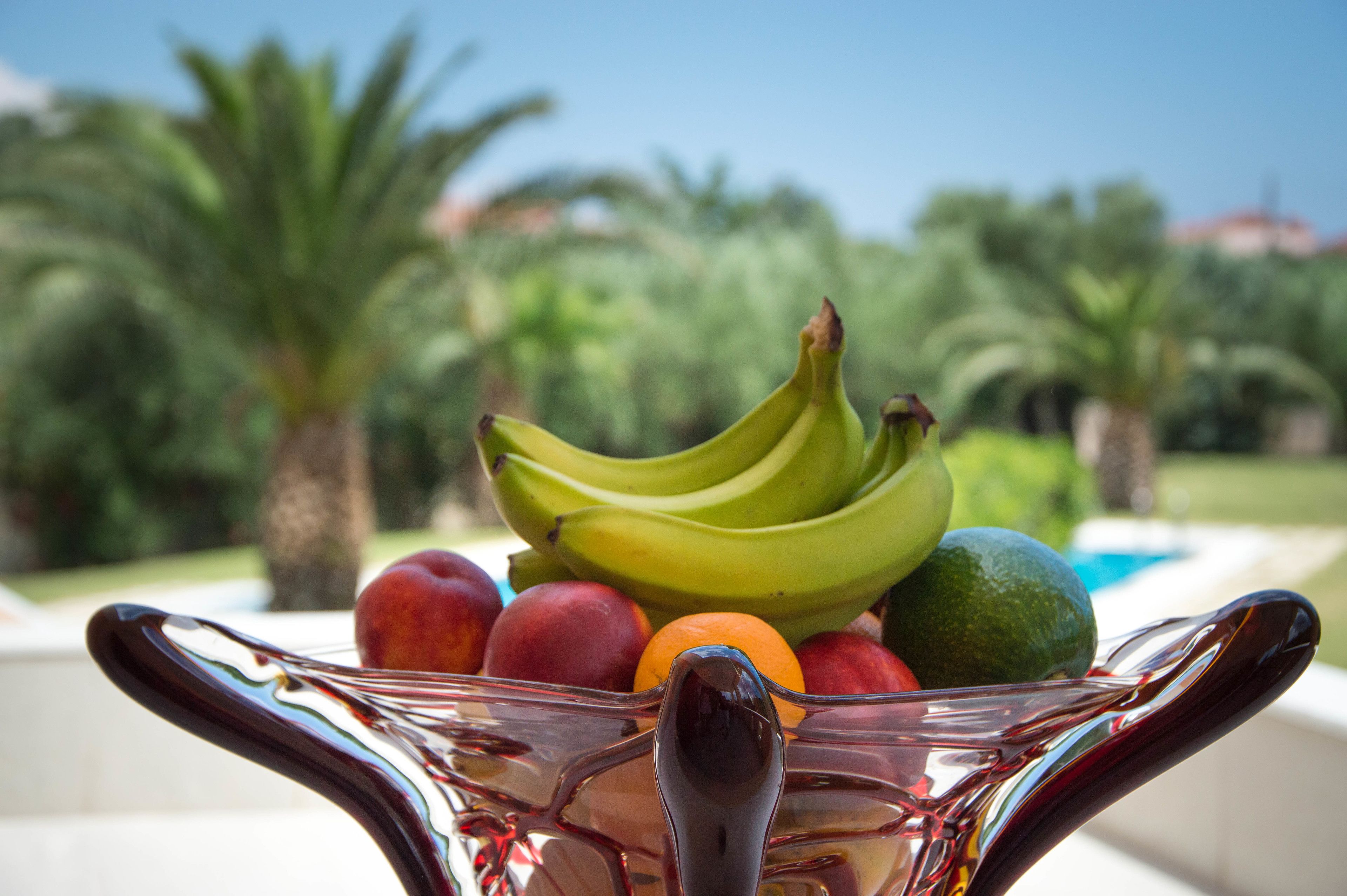 A fruit bowl with bananas, apples, oranges, and a lime on a reflective surface.