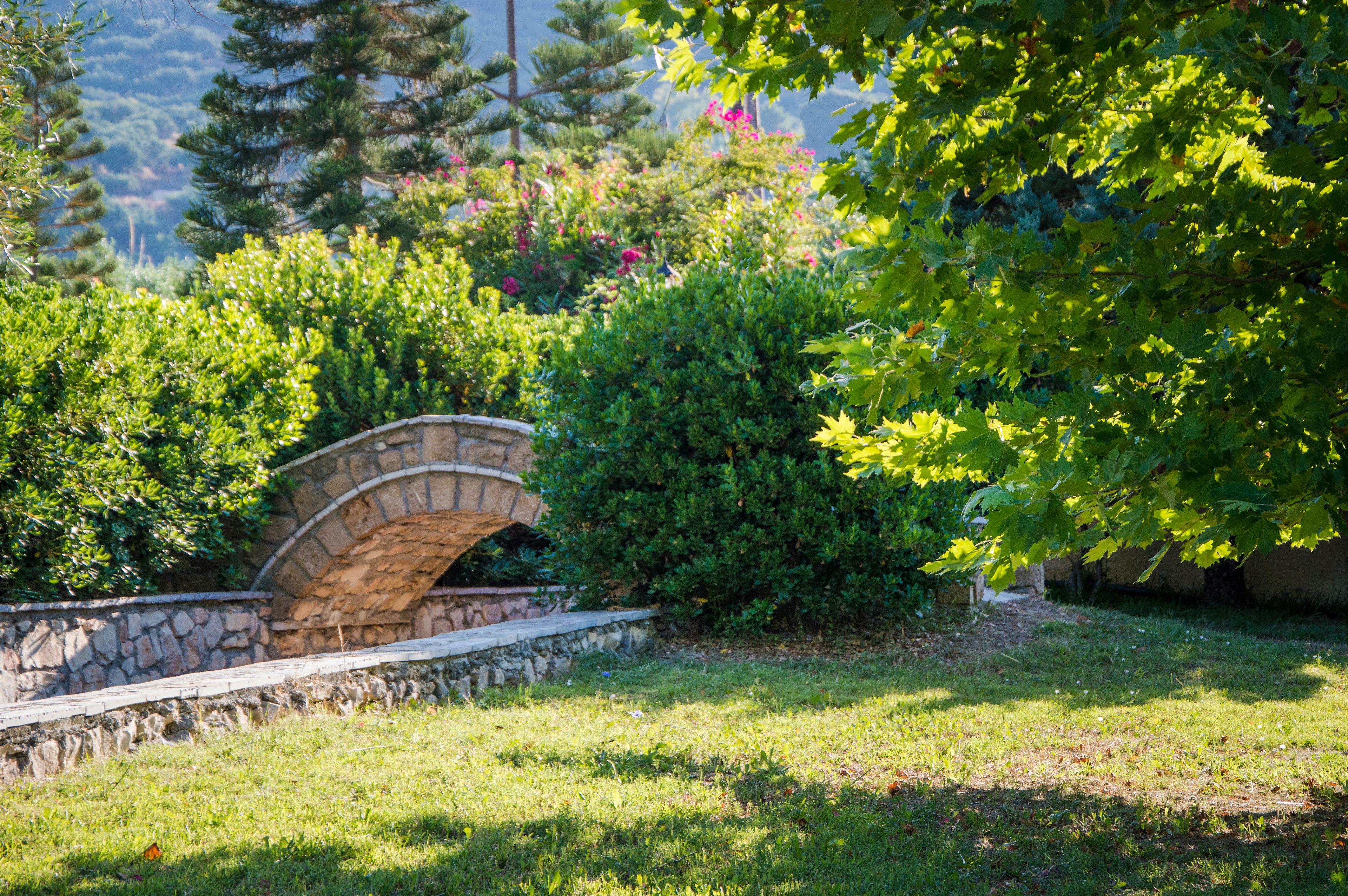 A stone bridge in a lush garden with dense foliage and a stone wall.