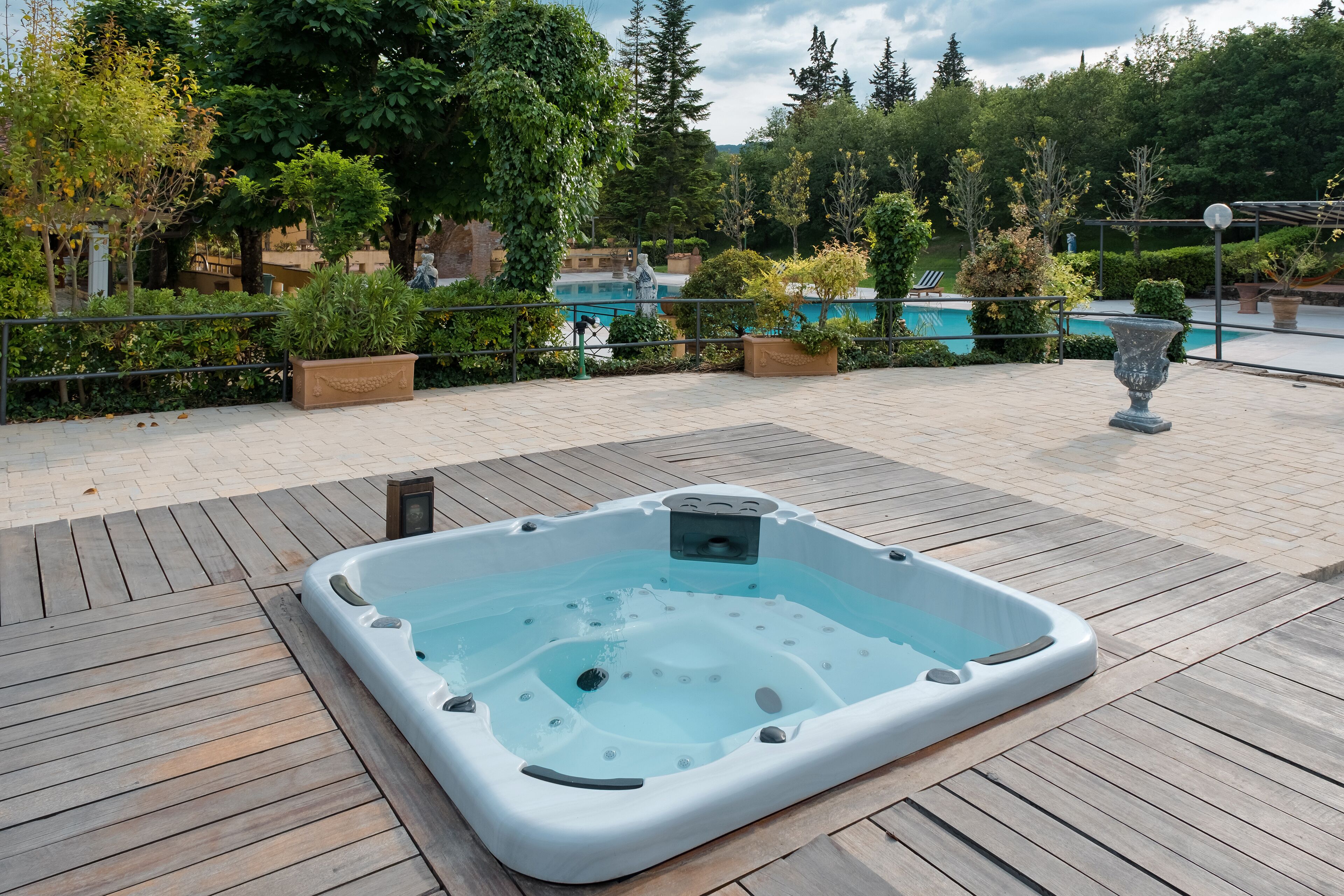 A hot tub on a wooden deck with a pool in the background.