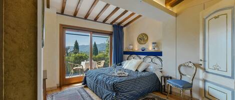 Un dormitorio con un ventanal grande, una cama con colcha azul y blanca a rayas, techo de madera y vistas al exterior.