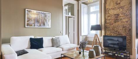 Een woonkamer met een witte bank, een glazen salontafel, een televisie en een kroonluchter.