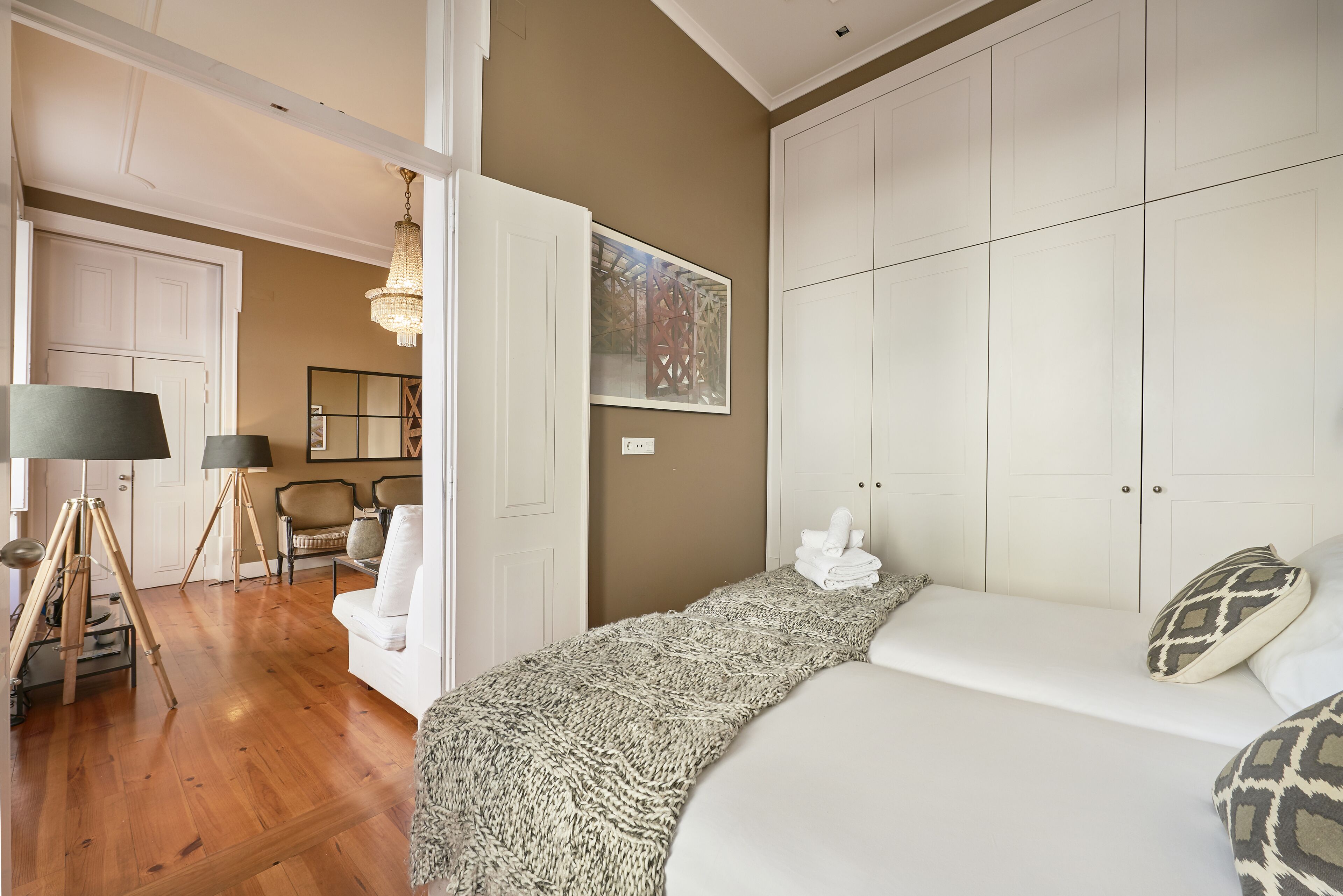 A bedroom with a large bed, a wardrobe, a chandelier, and a view of the hallway.