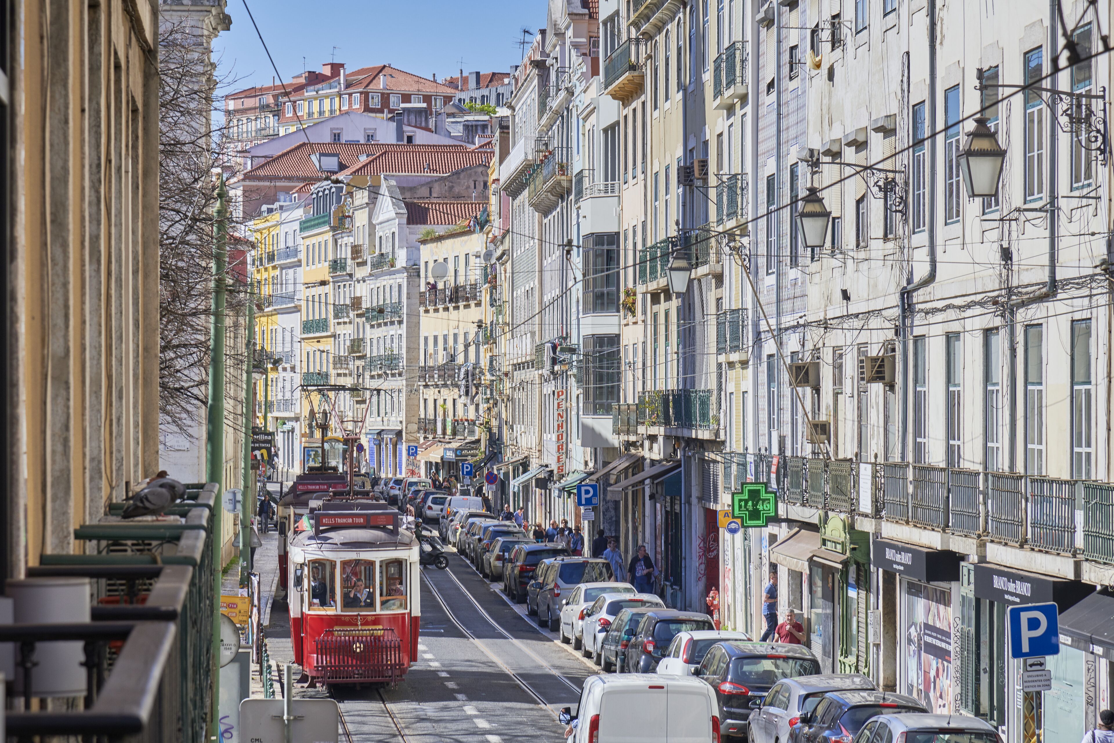 A narrow street lined with colorful buildings, parked cars, and a tram.