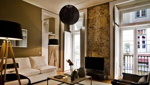 A living room with a sofa, coffee table, TV, and a balcony with a stone wall. - Lisbon Five Stars Apartments São Paulo 55 (Lisbon)