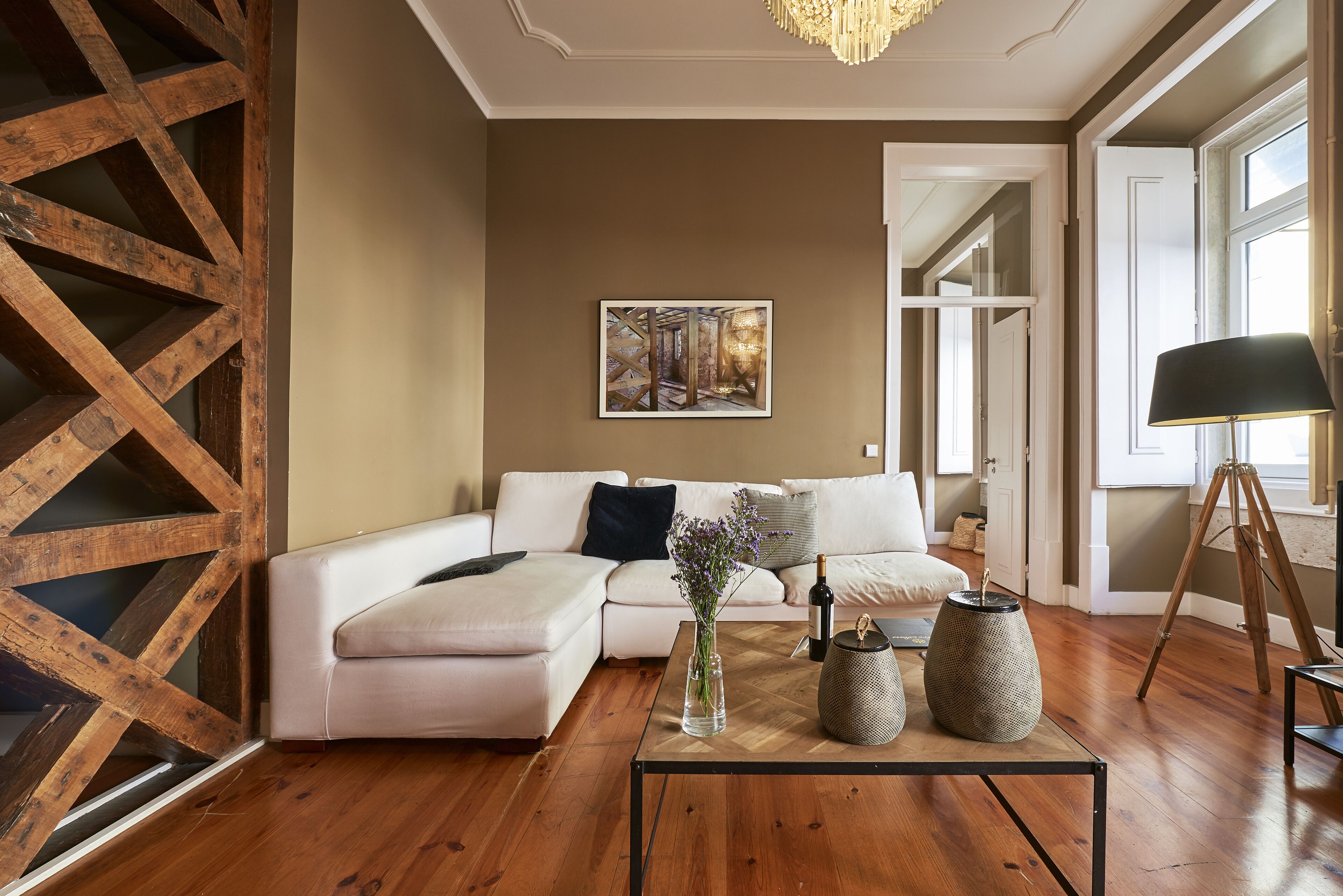 A modern living room with a wooden floor, a white sectional sofa, a coffee table with decorative items, and a painting on the wall.