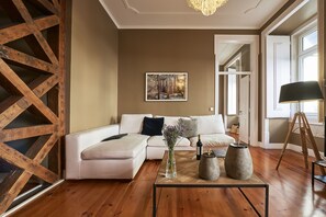 A modern living room with a wooden floor, a white sectional sofa, a coffee table with decorative items, and a painting on the wall.