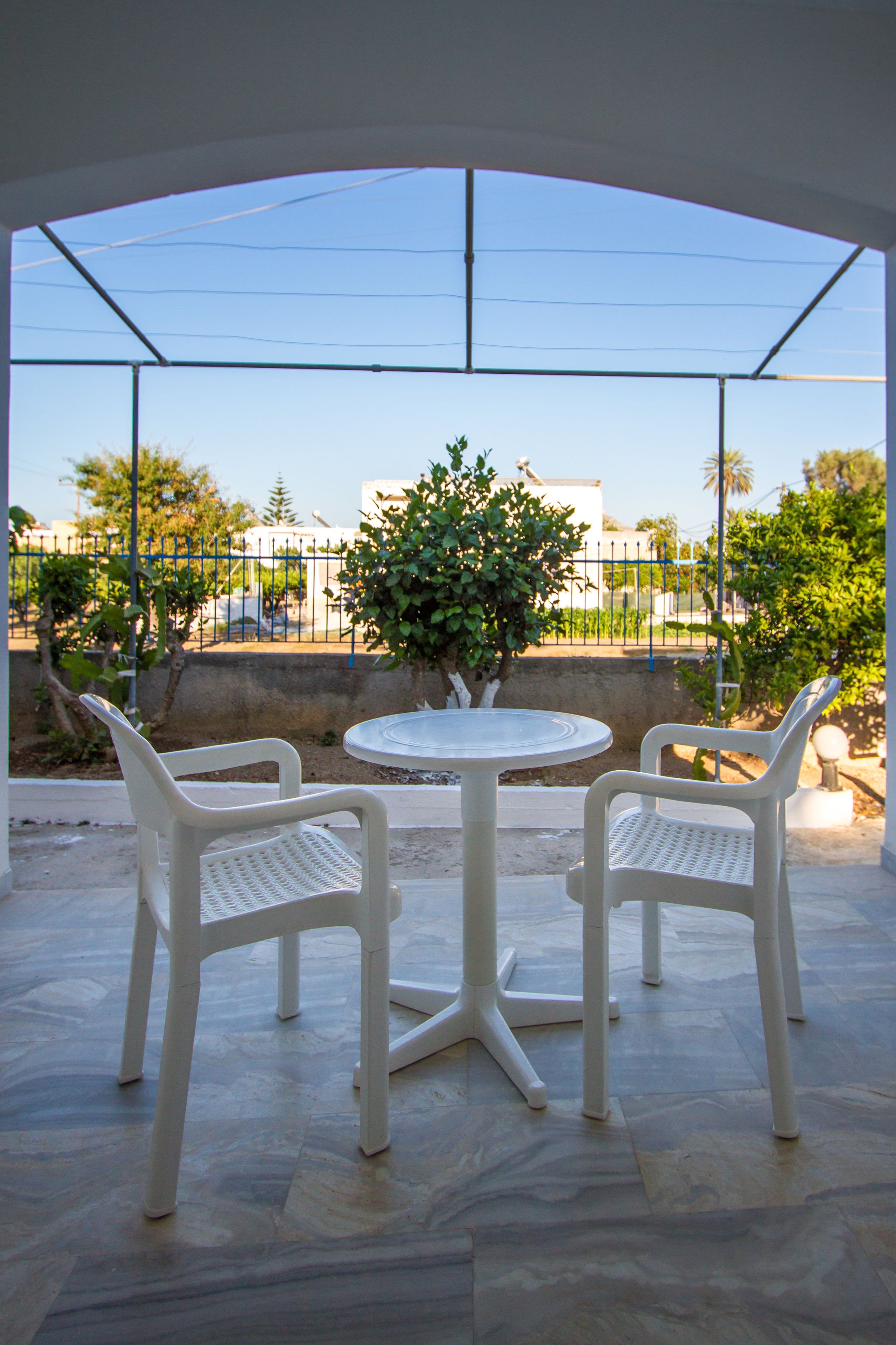 Een overdekt terras met een ronde tafel en twee witte plastic stoelen.