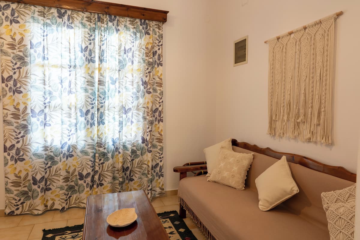 Una habitación con un sofá, una mesa de madera, una cortina estampada y un tapiz de macramé.