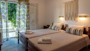 A double bed with a wooden frame, two bedside tables, a macrame wall hanging, and a view of greenery through a glass door. - Irene Hotel (Leros)