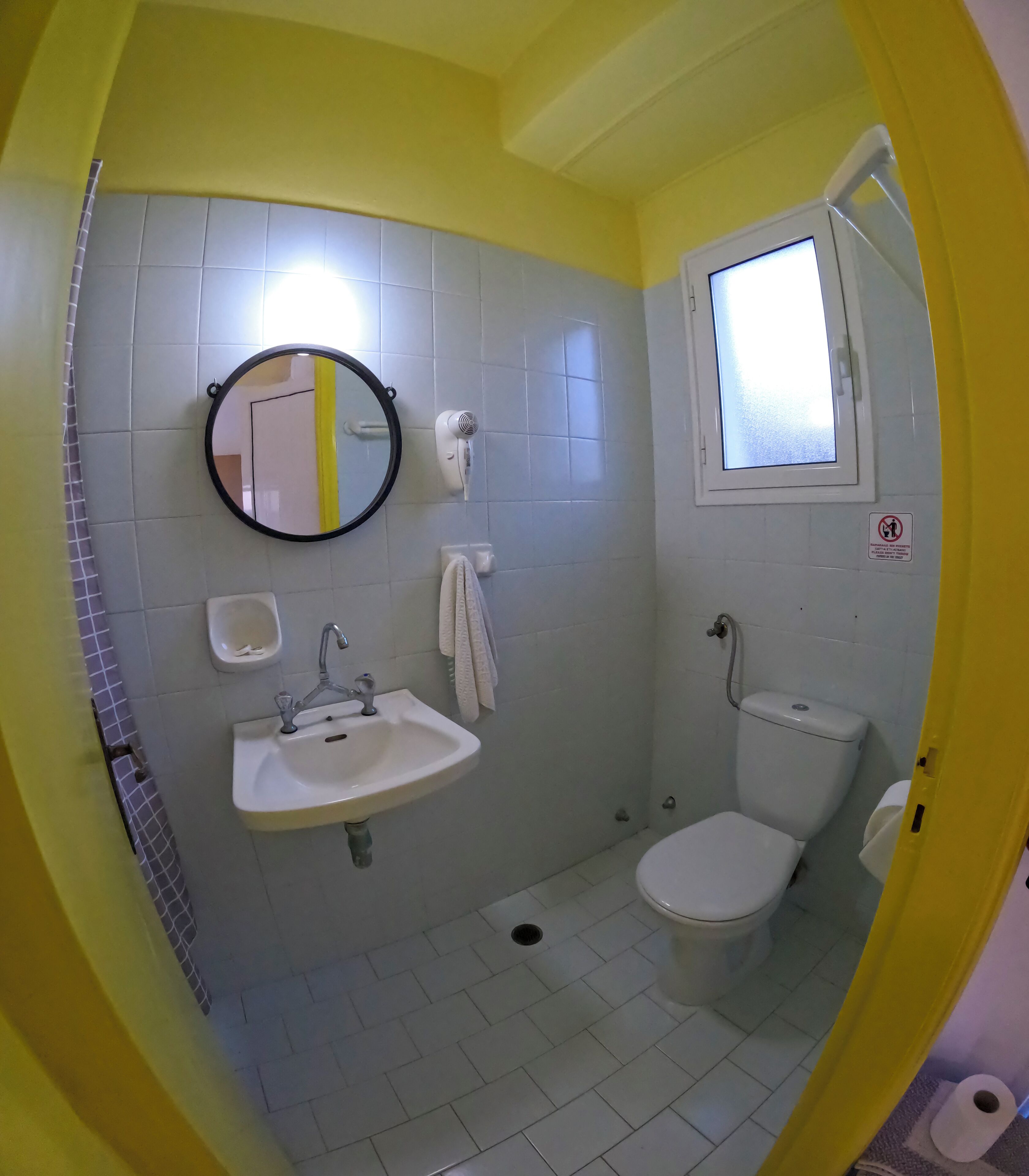 A bathroom with a sink, mirror, toilet, and a window.