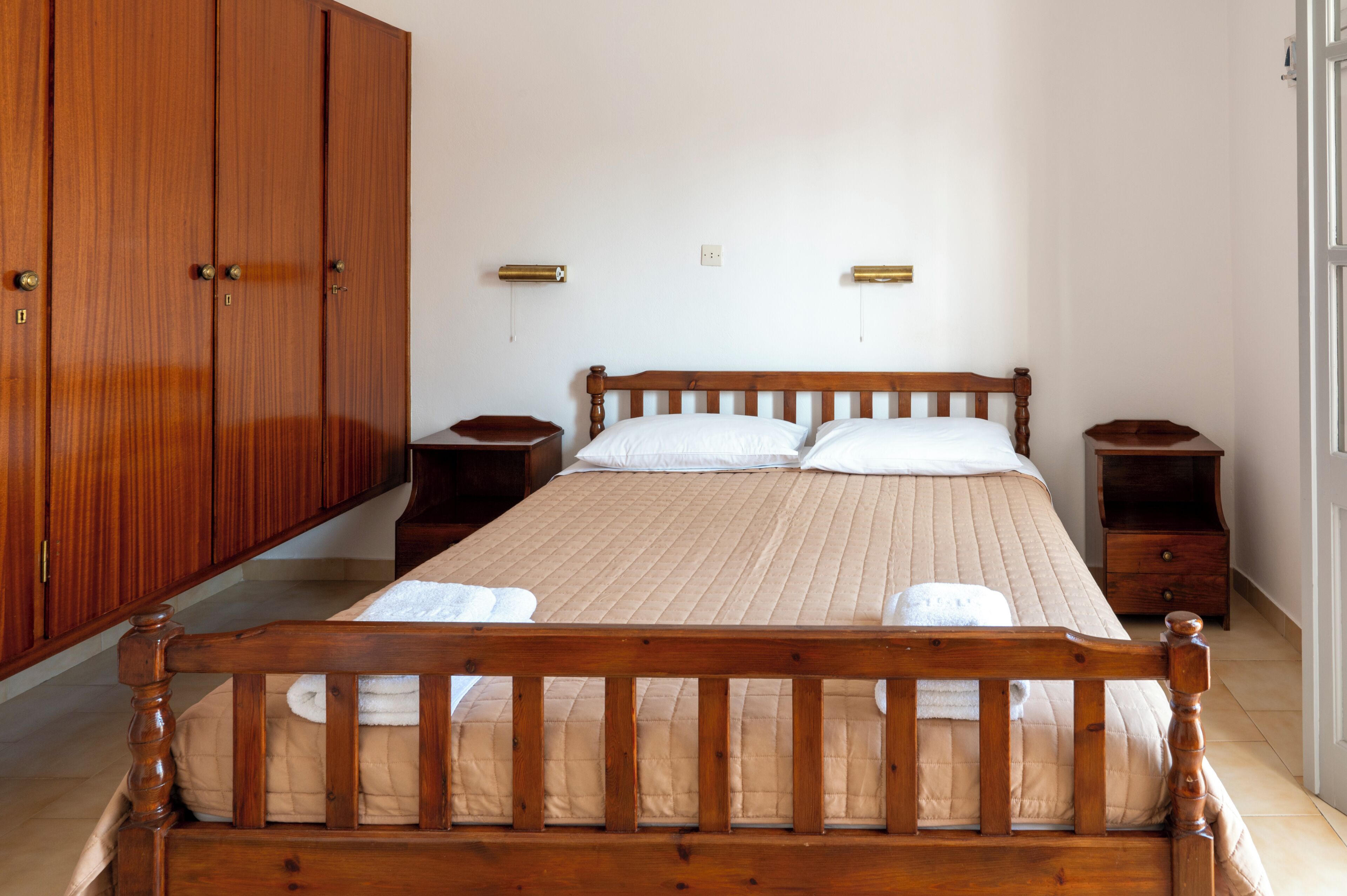 Ein Schlafzimmer mit einem hölzernen Bett, zwei Nachttischen, einem Kleiderschrank und einer Wandleuchte.
