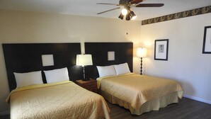 Quarto de hotel com duas camas, um ventilador de teto e duas luminárias de cabeceira.