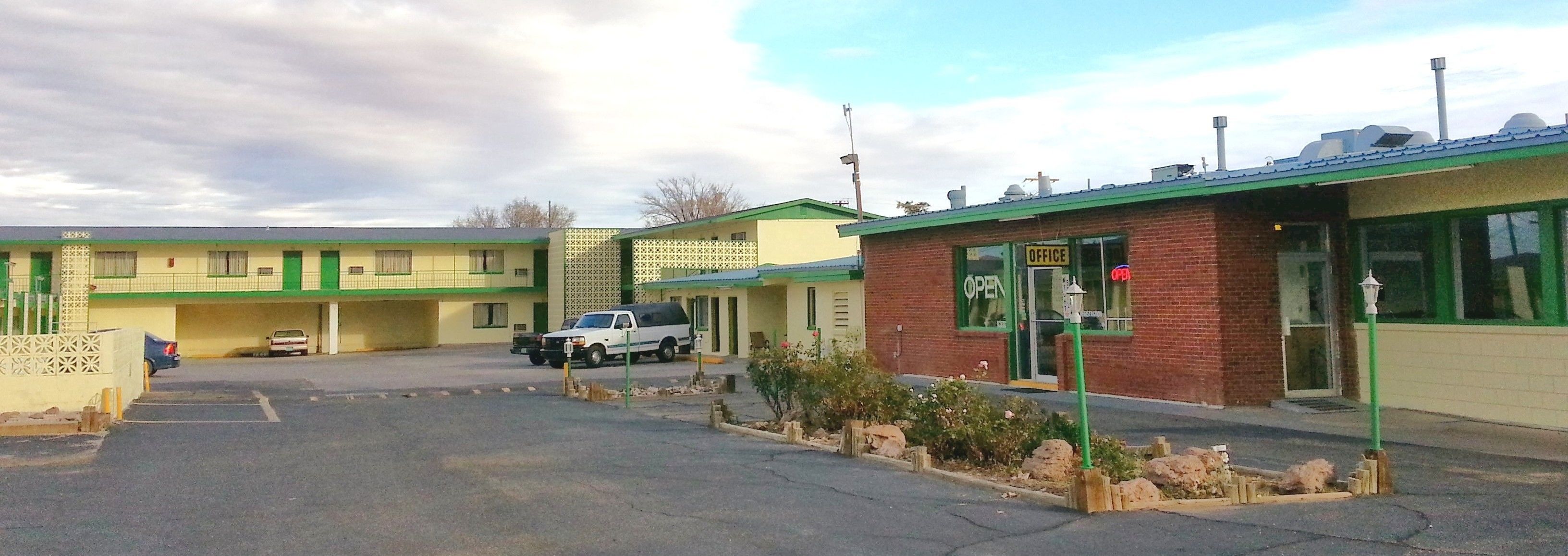 A motel with a green and yellow facade, a parking lot, and a small garden area.