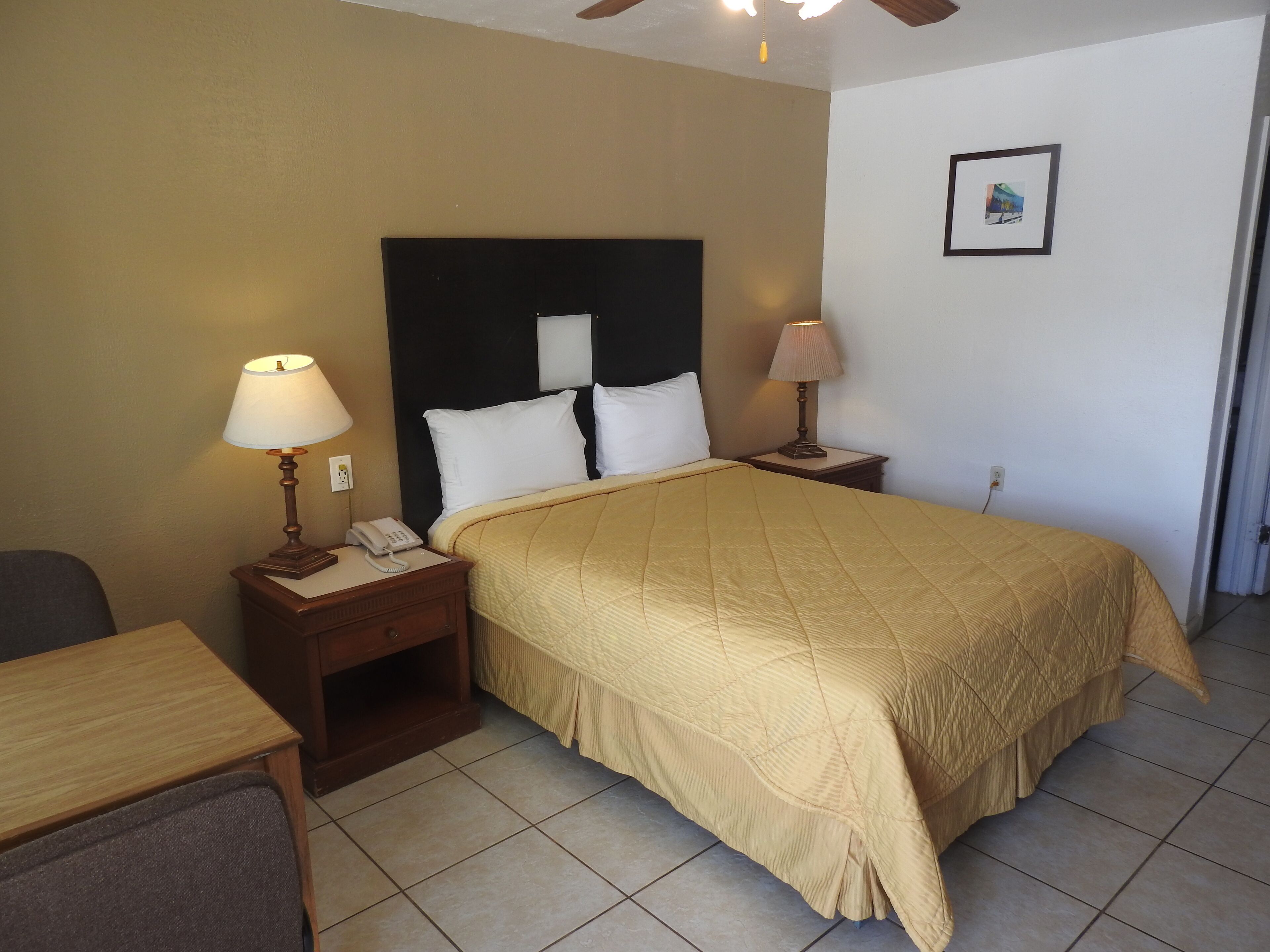 A hotel room with a bed, two bedside lamps, a telephone, a chair, and a framed picture on the wall.