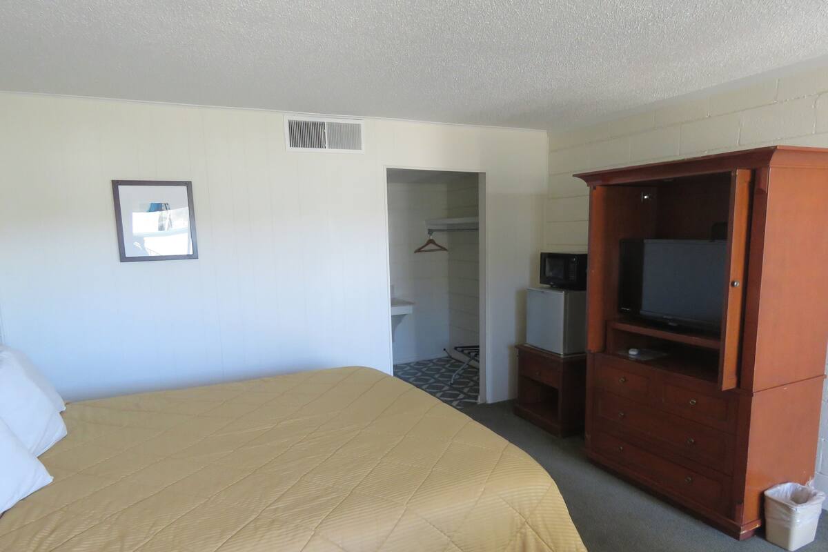 Ein Hotelzimmer mit einem großen Bett, einem Holzschrank, einem Fernseher und einer kleinen Küchenzeile.
