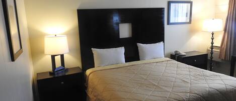 A hotel room with a large bed, two bedside tables, a nightstand, a lamp, a telephone, and a framed picture on the wall.
