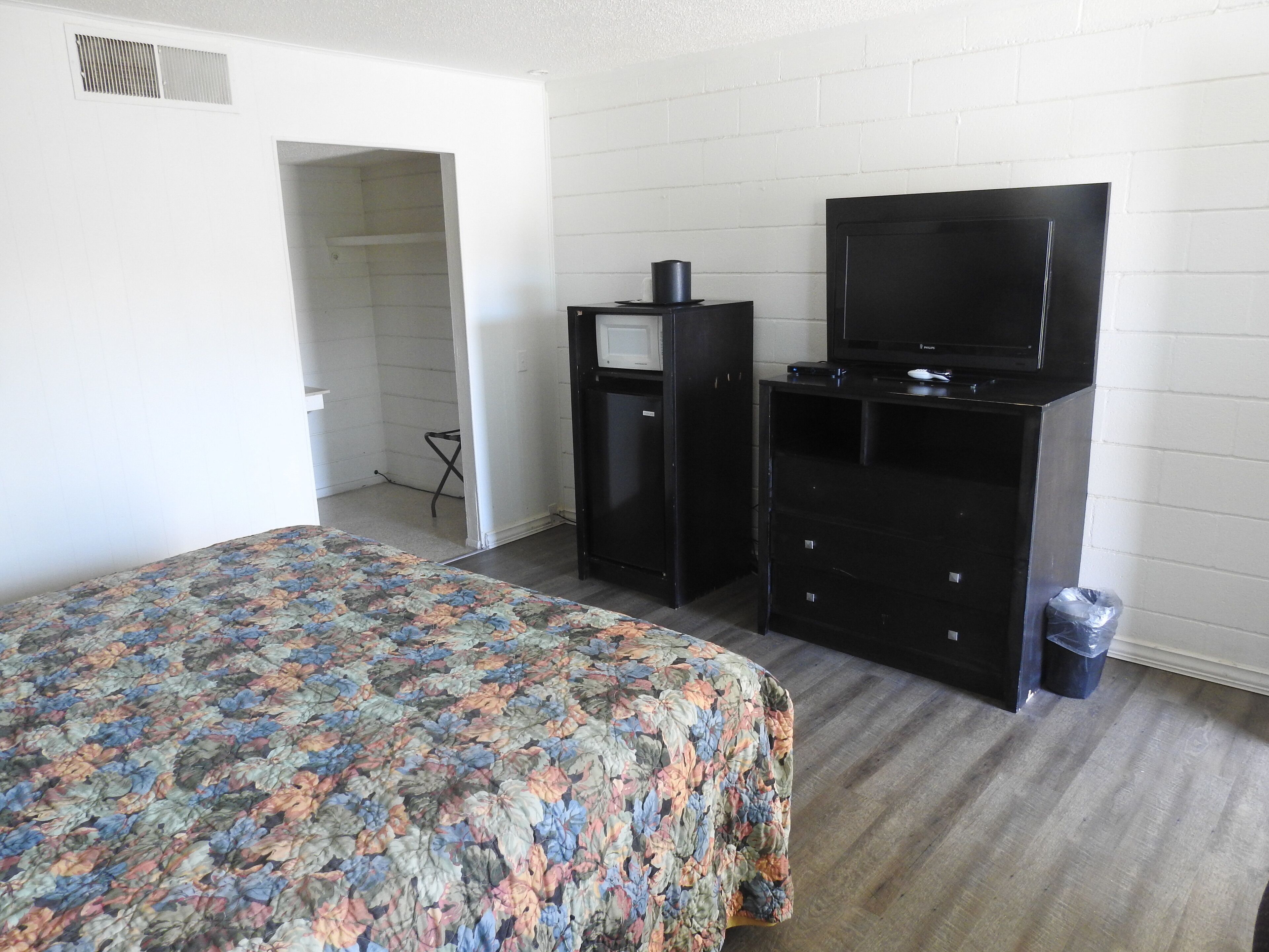 A hotel room with a bed, a TV, a dresser, and a trash bin.