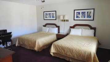 A hotel room with two beds, a desk, a chair, a ceiling fan, and artwork on the walls.