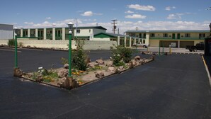 Um estacionamento com uma fileira de edifícios, uma cerca verde e algumas plantas.