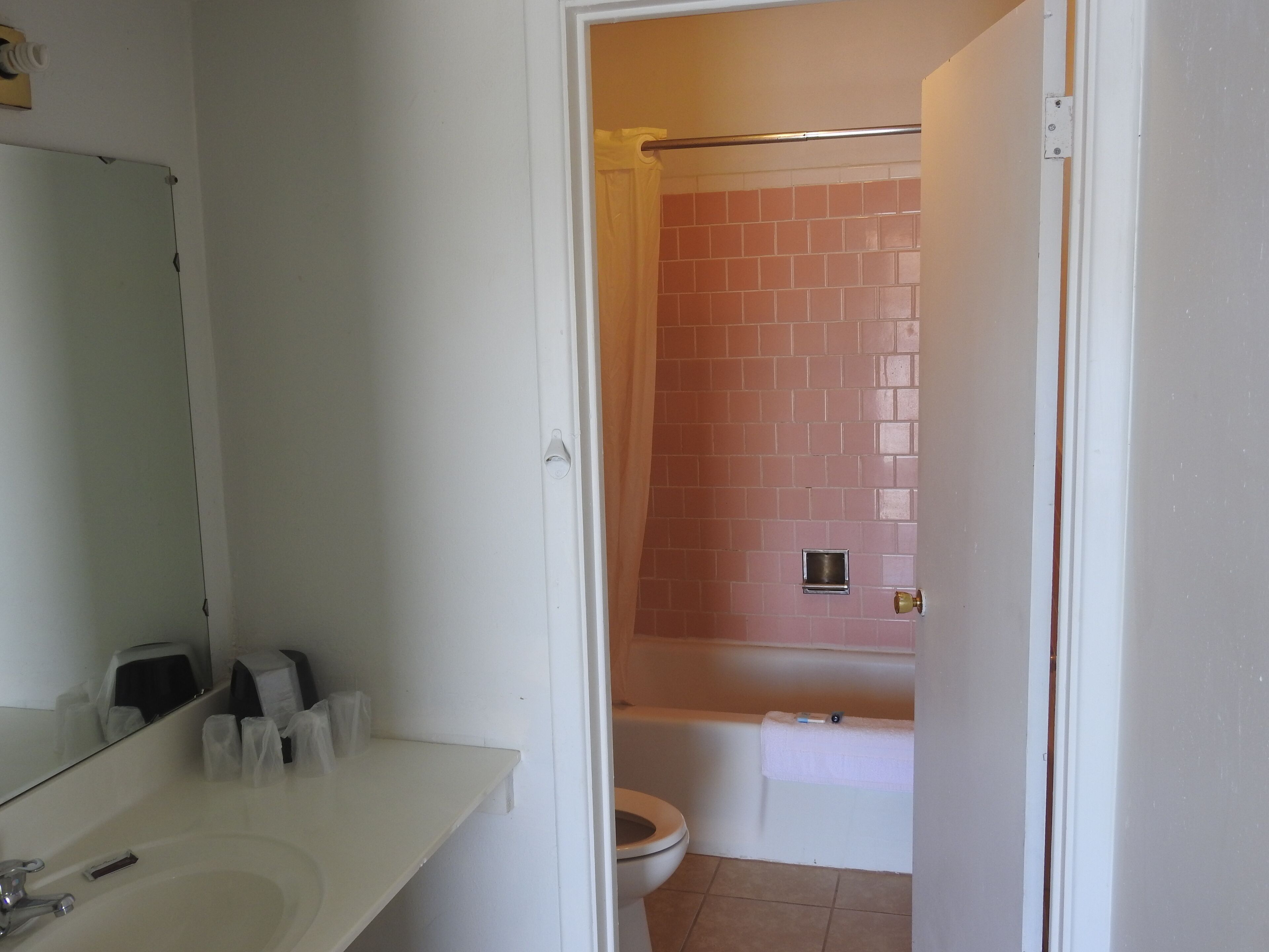 Un baño con lavamanos blanco, espejo y zona de ducha con azulejos rosados.