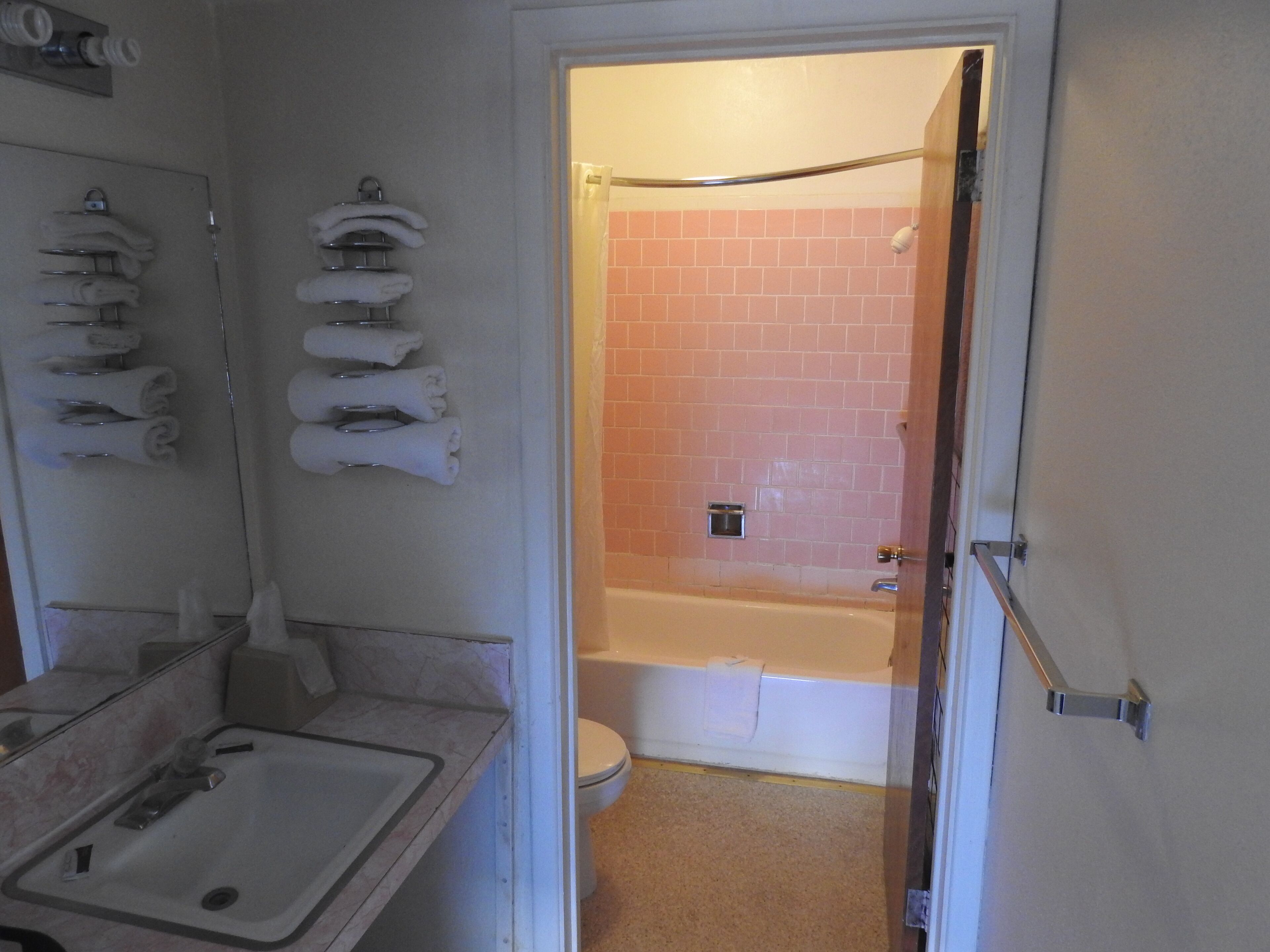 A bathroom with a sink, mirror, towel rack, and a shower area with pink tiles.