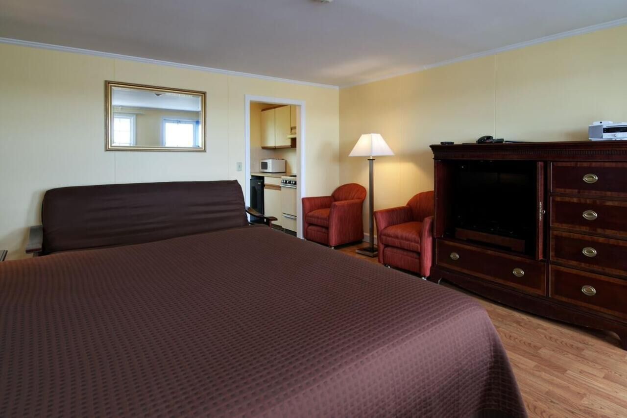 Une chambre d’hôtel avec un grand lit, une commode en bois, un bureau, une chaise, une lampe et un miroir.