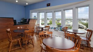A restaurant with wooden tables and chairs, a counter with a cash register, and large windows offering a view of the outside. - Cape Cod Harbor House Inn (Hyannis)