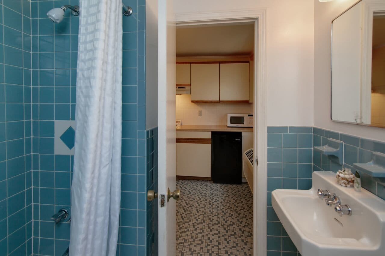 A bathroom with blue tiles, a shower, a sink, and a mirror.