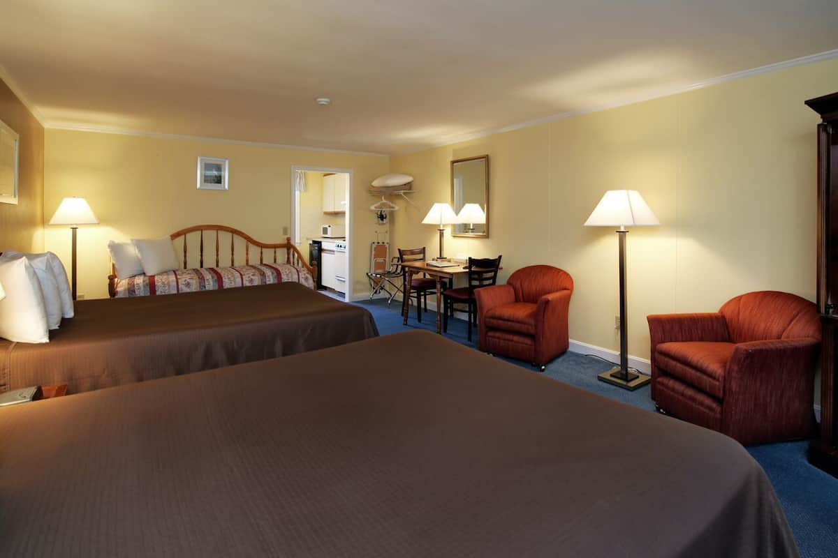 A hotel room with two beds, a desk, two chairs, and a lamp.