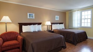 A hotel room with two beds, a red armchair, and a window with curtains. - Cape Cod Harbor House Inn (Hyannis)