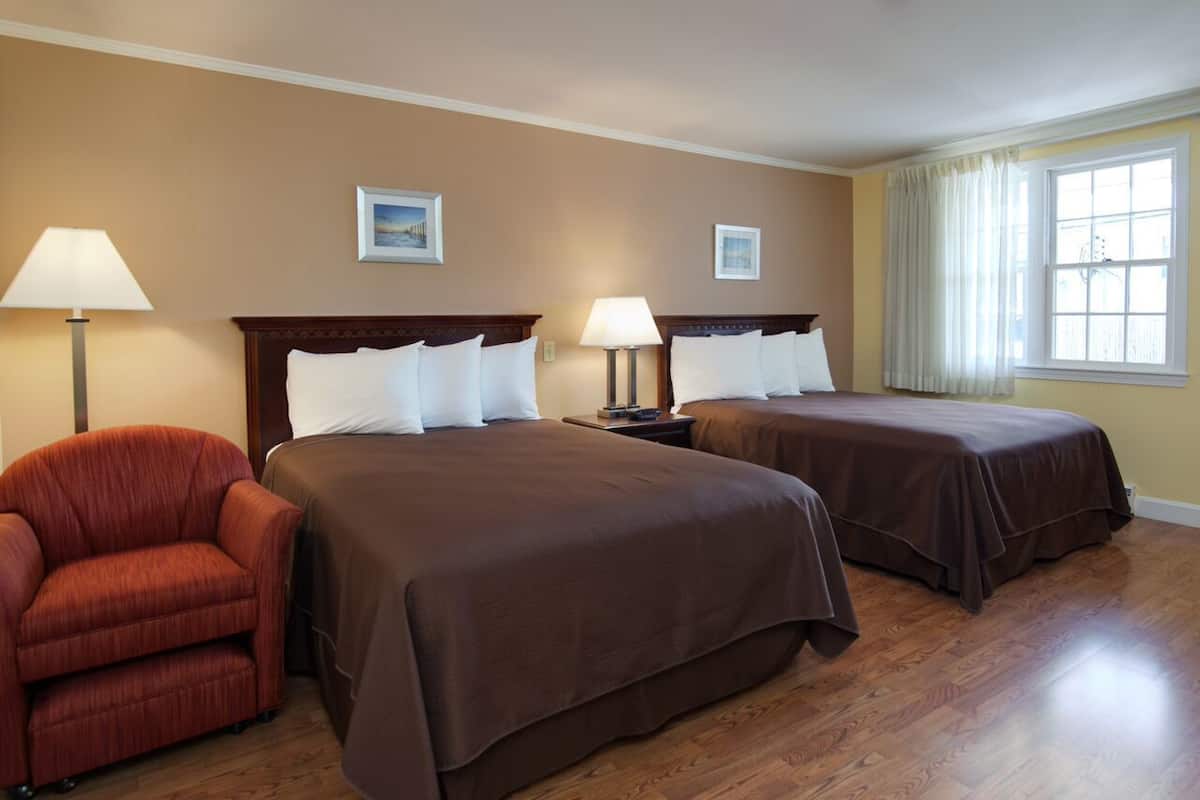 A hotel room with two beds, a red armchair, and a window with curtains.